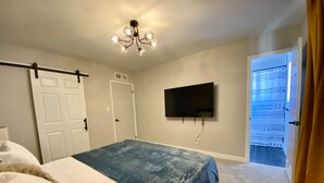 Un dormitorio con una cama, un televisor montado en la pared y una puerta que da a otra habitación.