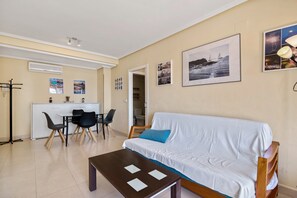Un salon avec un canapé blanc, une table à manger avec des chaises, un coin cuisine et un couloir.