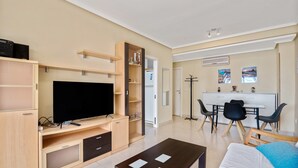 Ein modernes Wohnzimmer mit Flachbildfernseher, Holzmöbeln, einem Essbereich mit Stühlen und einer Küchenzeile.