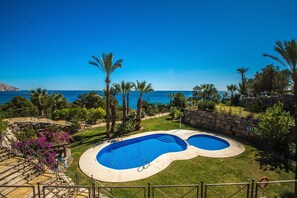 Una piscina con vista al mar, rodeada de palmeras y un muro de piedra.