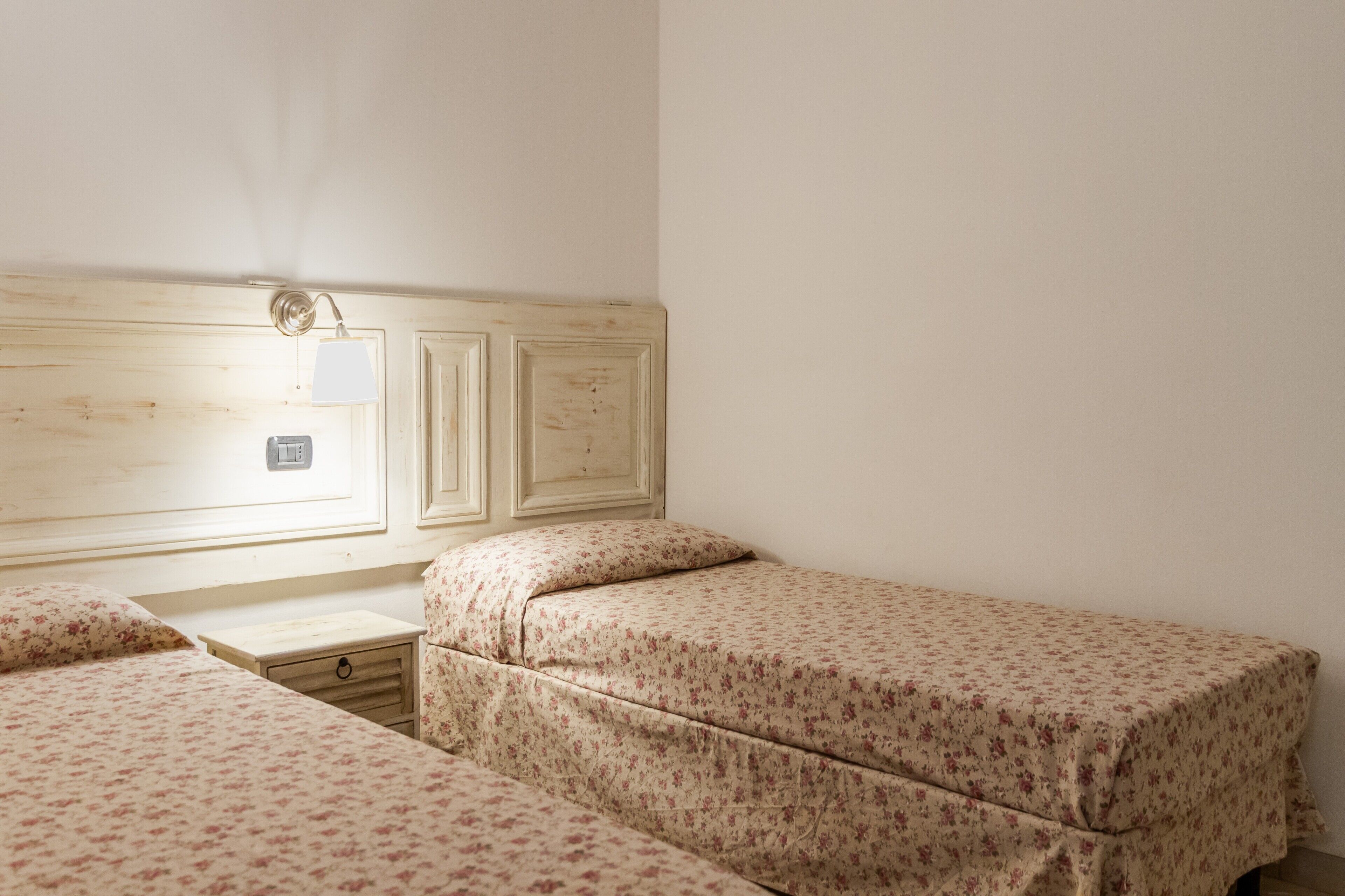 Une chambre avec deux lits, une tête de lit en bois, une table de chevet et un luminaire fixé au mur.
