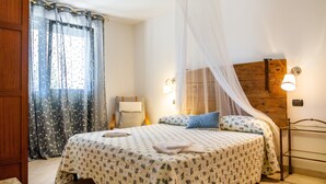 A bedroom with a bed, a bedside table, a chair, a nightstand, a wooden headboard, and a window with curtains. - Villa "Glicine - Colleberto" with Sea View, Private Terrace & Wi-Fi (Follonica)