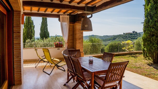 A covered patio with a wooden table and chairs, a hanging light fixture, and a view of a green landscape. - Villa "Glicine - Colleberto" with Sea View, Private Terrace & Wi-Fi (Follonica)
