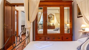 A bedroom with a large wooden wardrobe, a bed with a neatly folded white towel, and a bedside table with a lamp. - Villa "Bouganville - Colleberto" with Sea View, Private Terrace & Wi-Fi (Follonica)