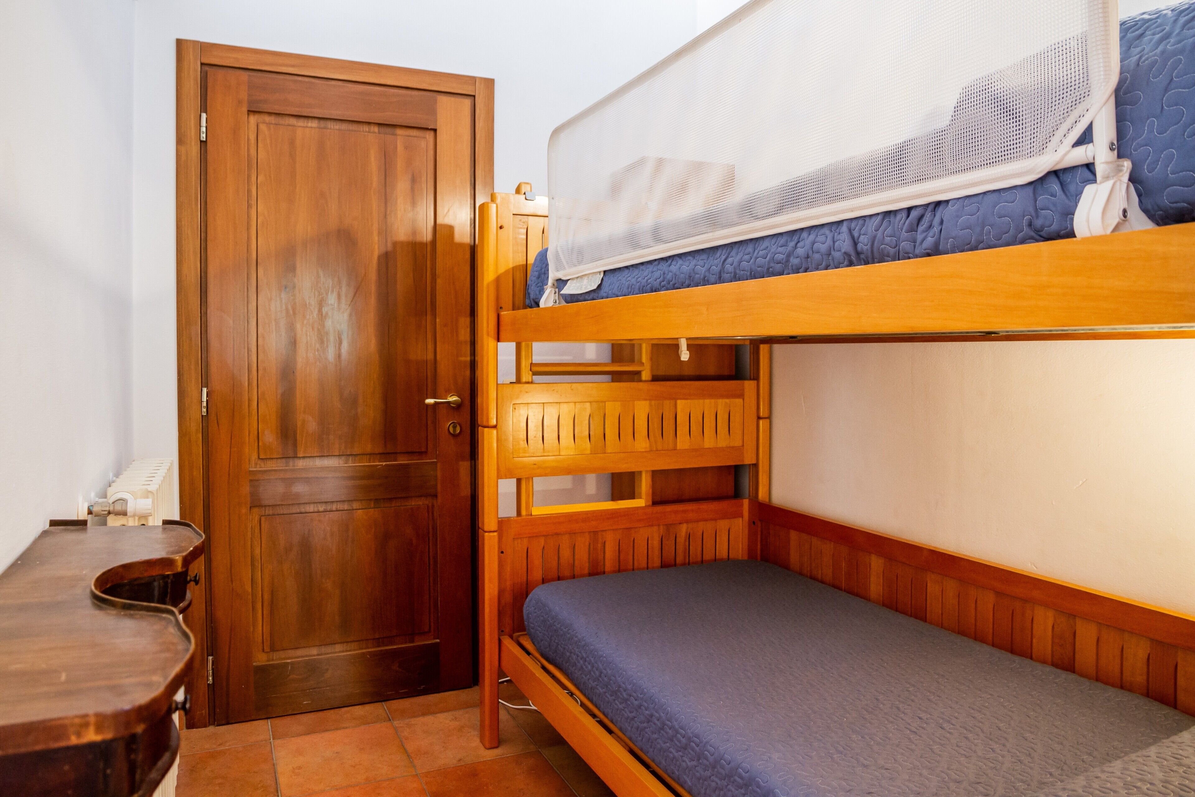 A bunk bed with a wooden headboard, a lower bunk with a blue mattress, and a door with a wooden frame.