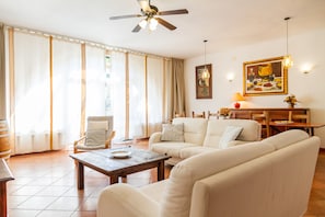 A living room with a sofa, a wooden table, a chair, a ceiling fan, and a dining area with a table and chairs.