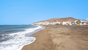 Una platja amb sorra, una muntanya al fons i edificis al llarg de la costa.