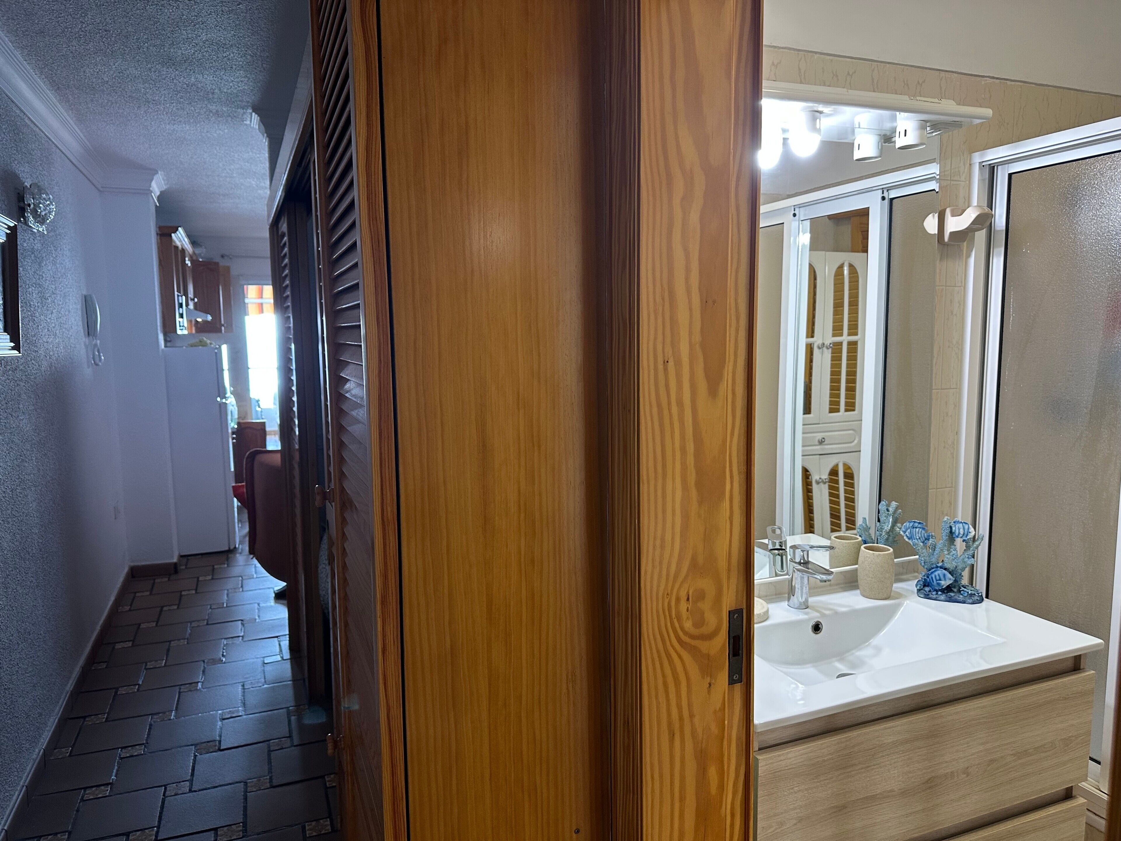 A hallway leading to a bathroom with a sink, mirror, and decorative items.