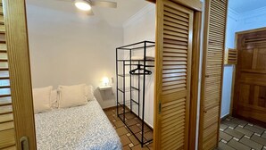 Ein Schlafzimmer mit Bett, Nachttisch, Kleiderstange und Deckenventilator.