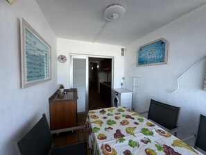 A small, compact room with a bed, a desk, a chair, a radiator, and a door leading to another room.