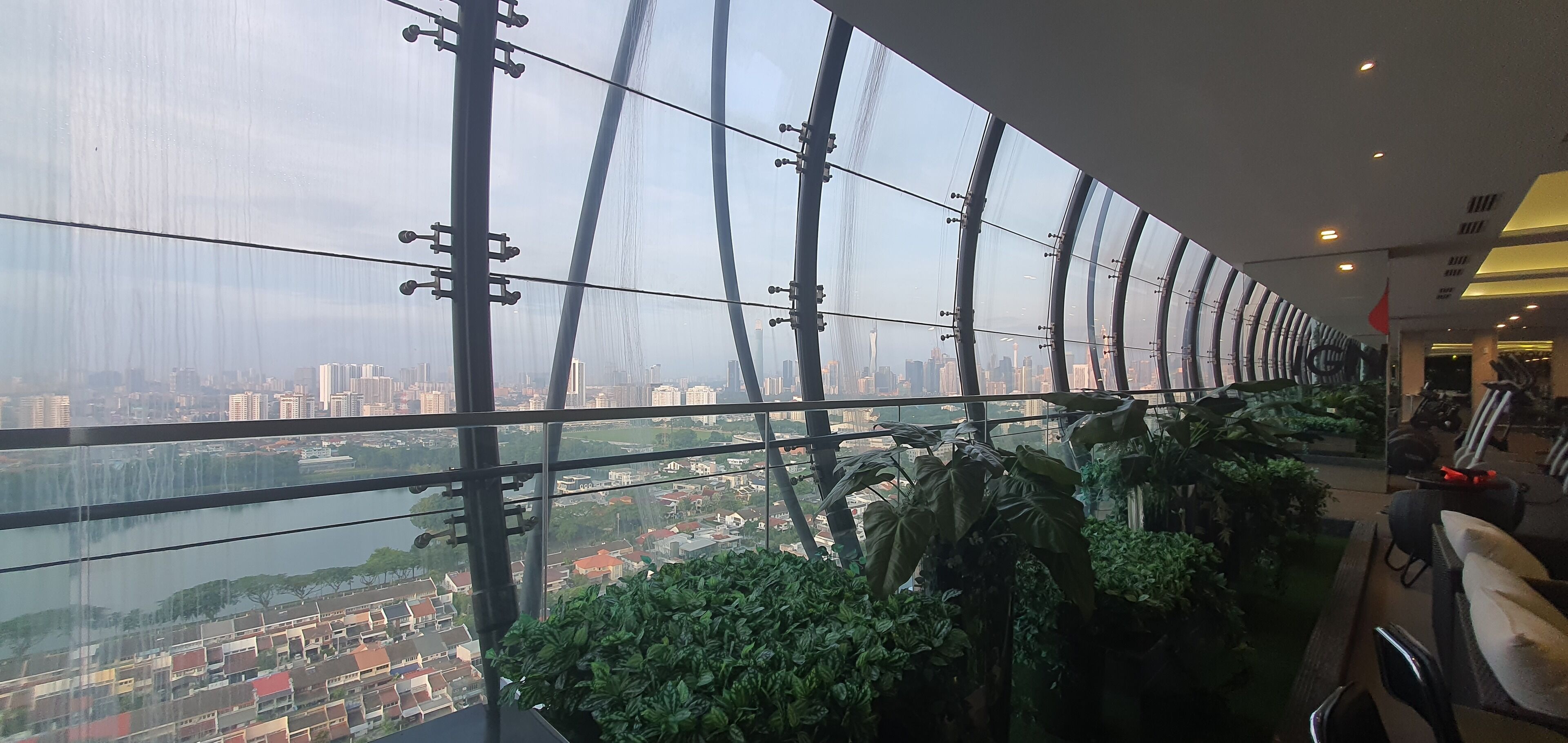 A high-rise hotel interior with a panoramic city view, large windows, and indoor plants.