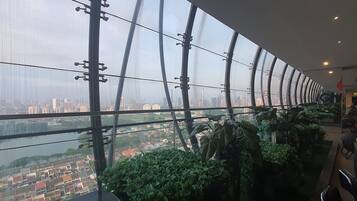 A high-rise hotel interior with a panoramic city view, large windows, and indoor plants.