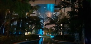 ’s Nachts uitzicht op een hotel met een zwembad, palmbomen en een gebouw met verlichte ramen.