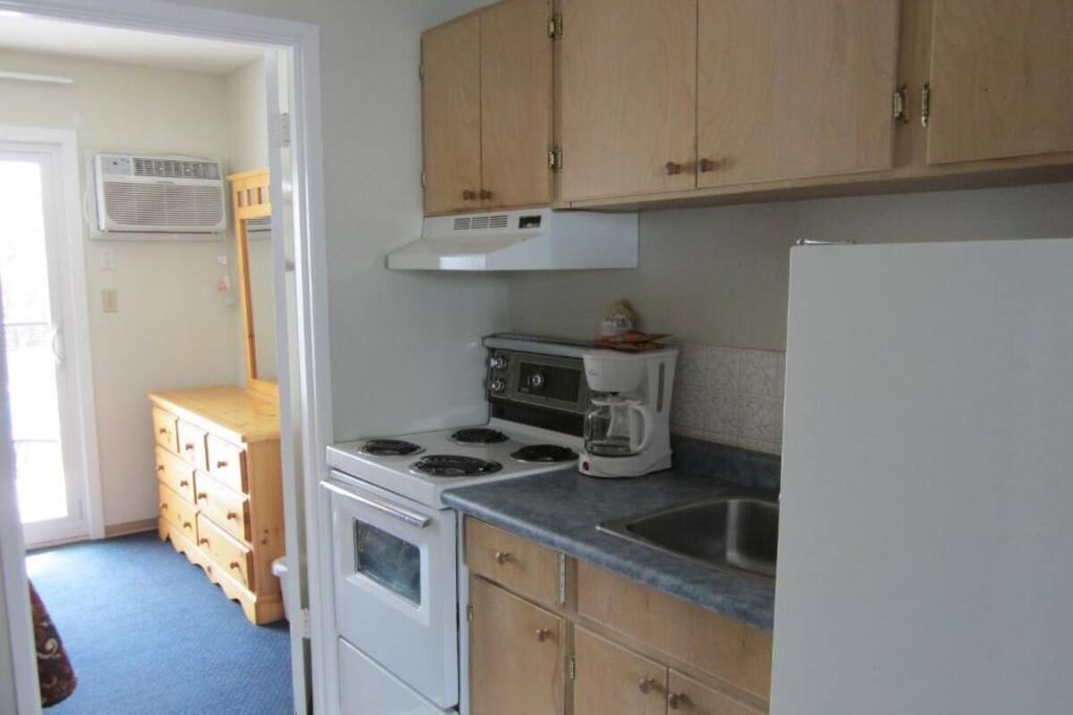 A compact kitchen with wooden cabinets, a white stove, a coffee maker, and a sink.