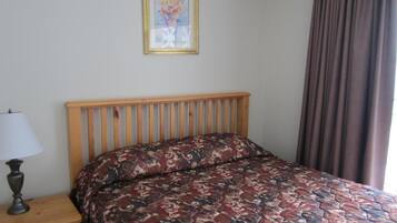 Une chambre à coucher avec une tête de lit en bois, une couvre-lit à motifs, une table de chevet avec une lampe et un tableau encadré accroché au mur.