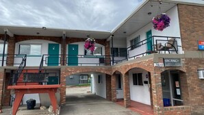 A two-story motel with a brick facade, a covered parking area, and hanging flower baskets. - Schell Motel (Vernon)