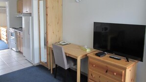 A compact living space with a kitchenette, a TV, a wooden desk, and a chair. - Schell Motel (Vernon)