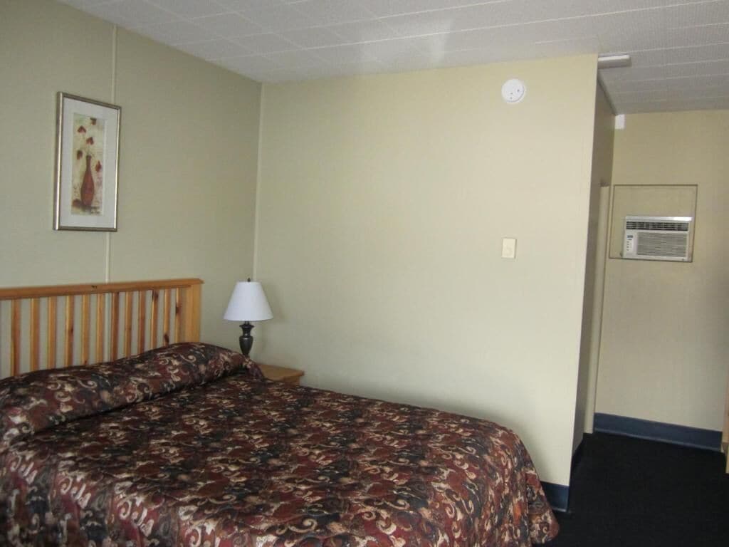 Habitación de hotel con cama, lámpara, aire acondicionado instalado en la pared y un cuadro enmarcado.