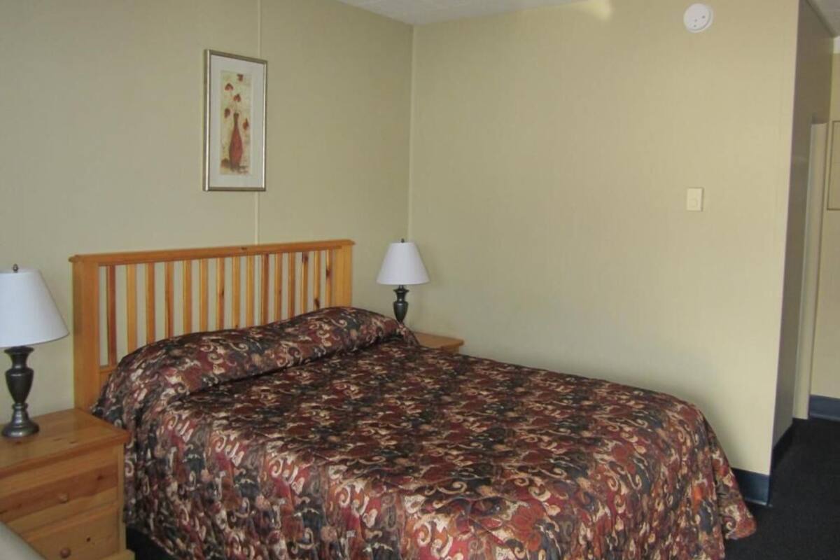 A bedroom with a wooden bed, two bedside lamps, a framed picture on the wall, and a door to the right.
