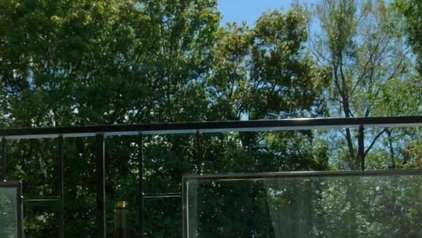 A glass-enclosed pool area with two empty wine glasses on a table, surrounded by a clear glass barrier. - Schell Motel (Vernon)