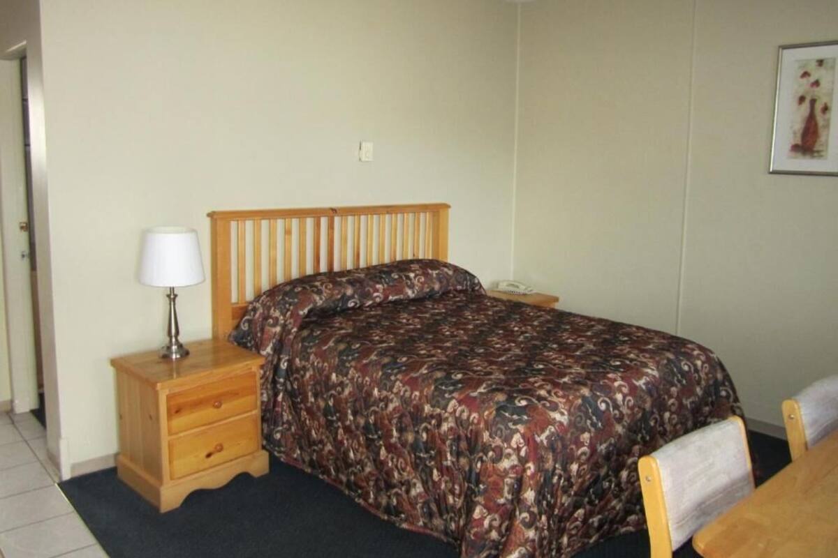 A bedroom with a wooden bed, a bedside table with a lamp, and a chair.