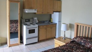 A compact kitchen with wooden cabinets, a stove, and a refrigerator. - Schell Motel (Vernon)
