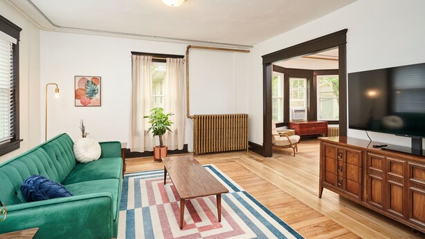 Uma sala de estar com um sofá verde, uma mesa de centro de madeira, uma televisão e um radiador.
