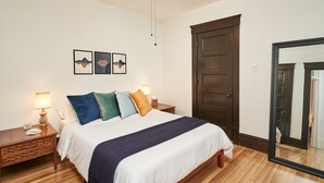 Quarto com cama, mesas de cabeceira, ventilador de teto e uma porta.