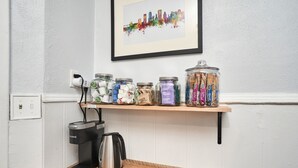 Uma bancada de cozinha com uma cafeteira, potes de condimentos e uma imagem enquadrada da paisagem urbana na parede.
