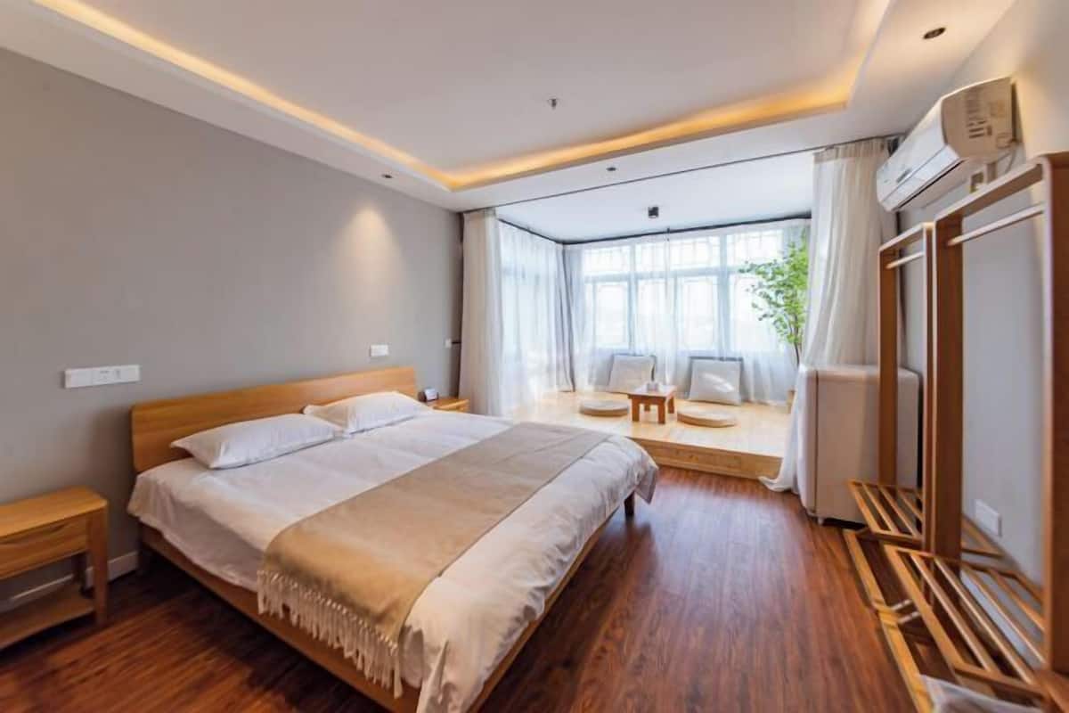 A modern hotel room with a large bed, a seating area with a view, and a wooden floor.