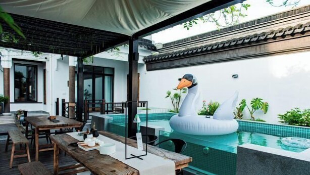 An outdoor dining area with wooden tables and benches, a swimming pool with a swan float, and a traditional tiled wall. - Suzhou Taihu Lakeside·Shanhu Yin·Holiday Homestay (Suzhou)