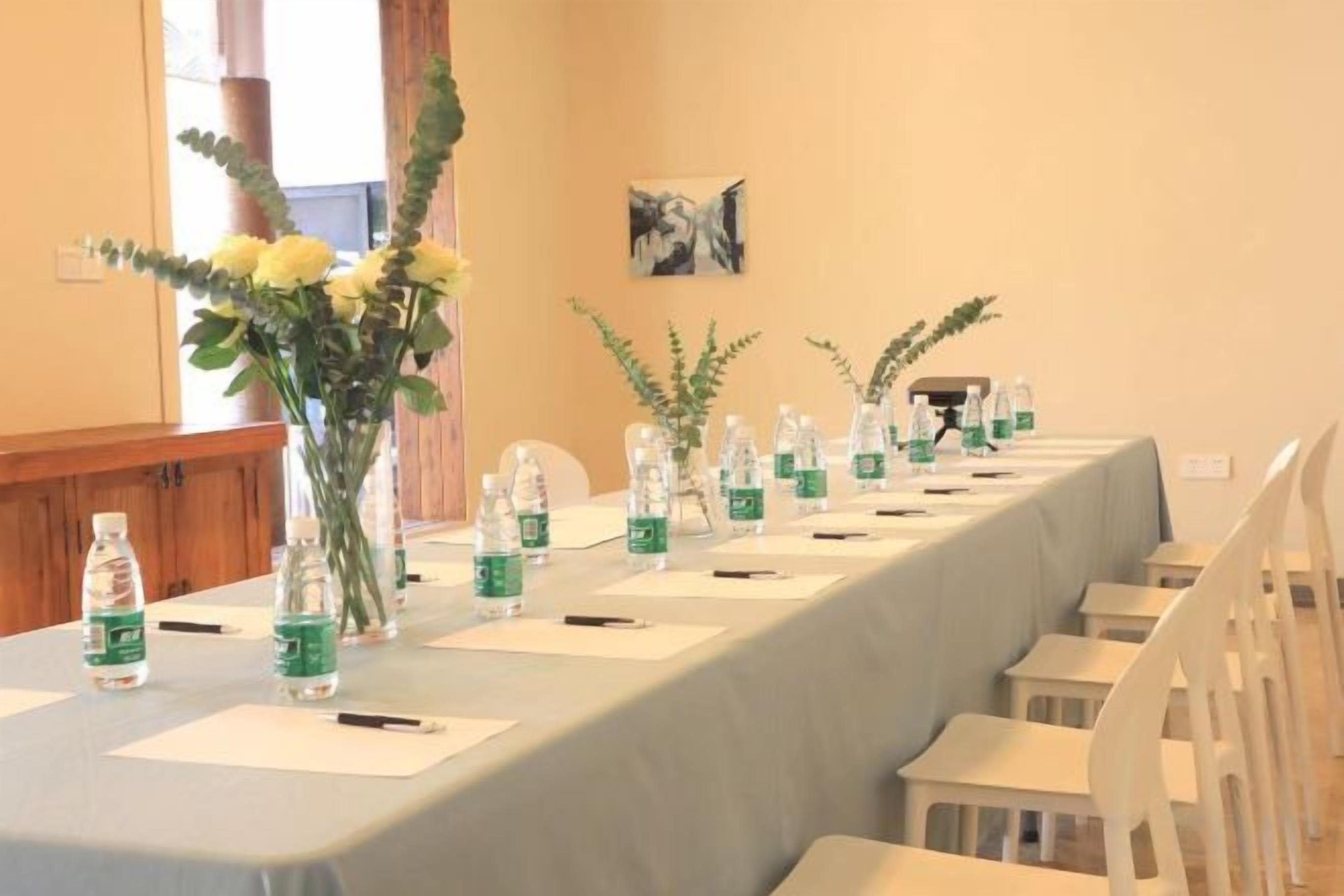 A conference table with water bottles, pens, and notepads, set in a room with chairs and a window.