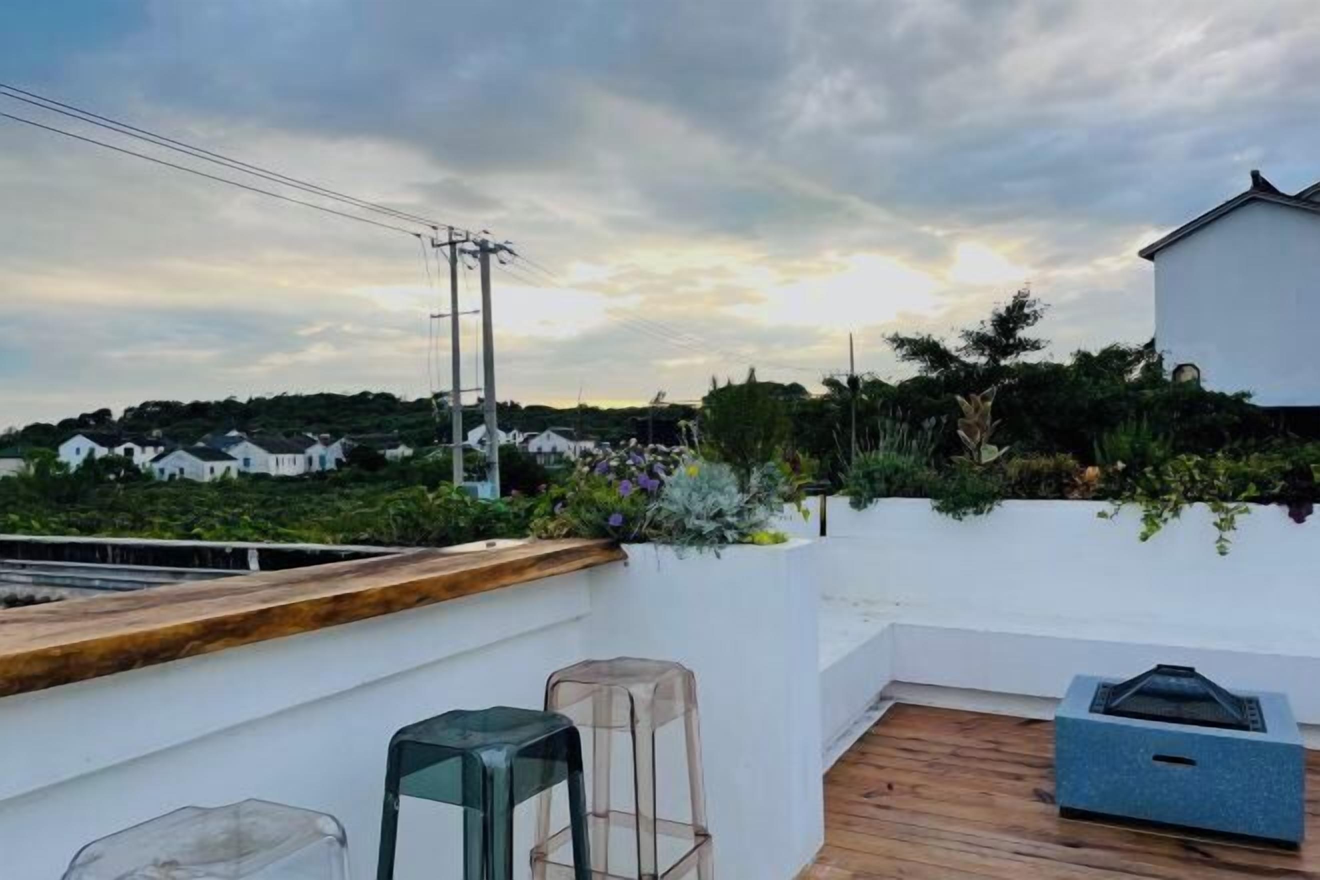 A rooftop terrace with a wooden deck, a white wall with a planter, and a clear glass table.