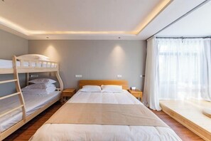 Une chambre d’hôtel avec un lit superposé, un lit simple, une table de chevet, une commode et une fenêtre avec des rideaux.