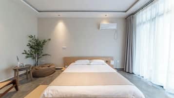 Una habitación de hotel moderna con una cama grande, una mesita de noche, una planta y una ventana con cortinas.