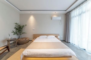 Una habitación de hotel moderna con una cama grande, una mesita de noche, una planta y una ventana con cortinas.