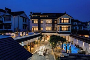 Une cour d’hôtel avec des espaces de détente en plein air et une piscine, le tout baigné par la lumière du crépuscule.