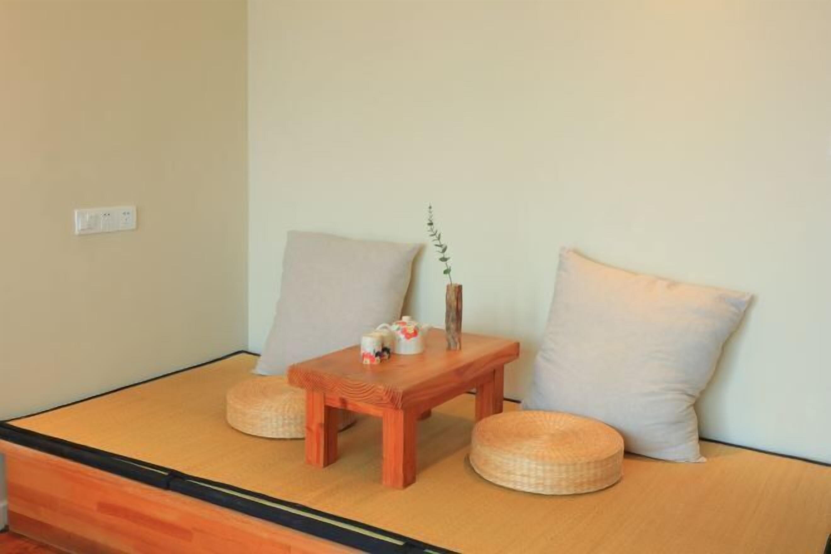 A tatami mat room with a low wooden table, two cushions, and a small vase with a plant.