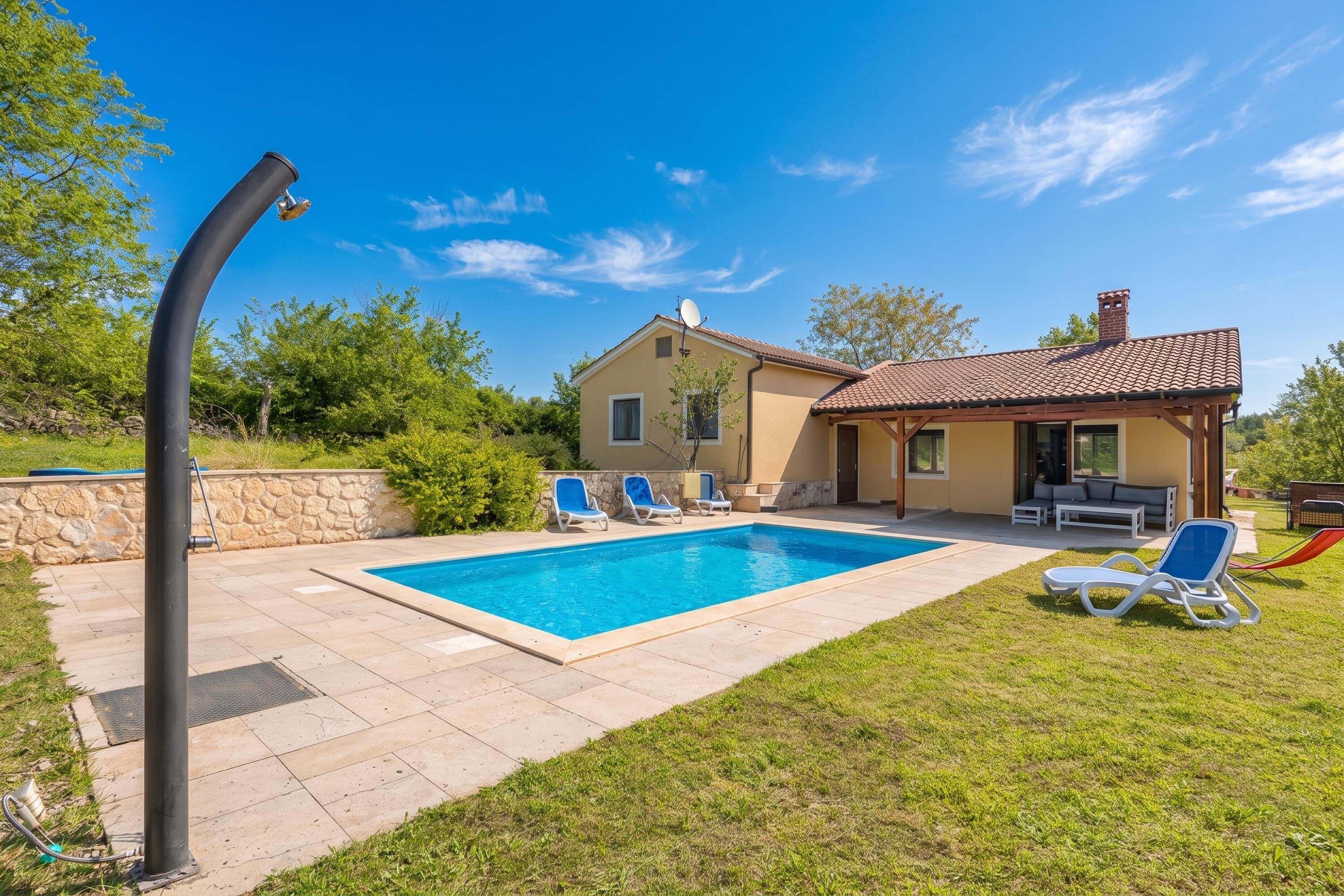 Una casa con piscina, sillas de descanso y un muro de piedra.