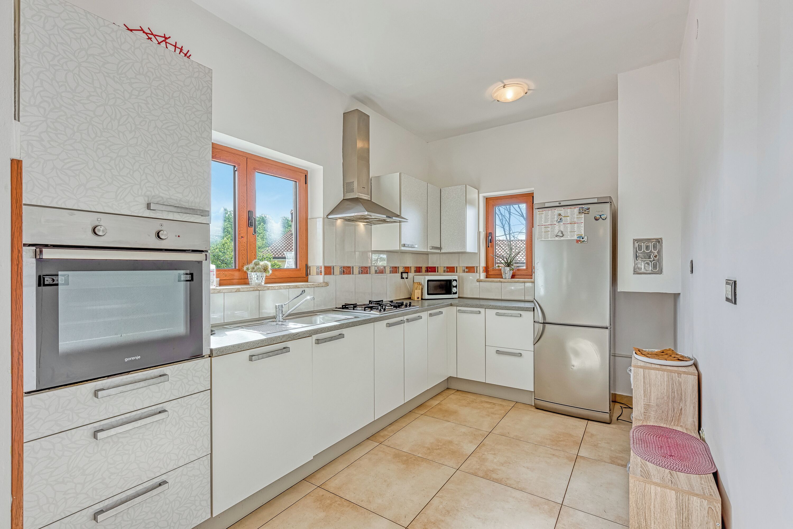 Una cocina moderna con horno empotrado, microondas y refrigerador, que cuenta con gabinetes blancos y un ventanal grande.