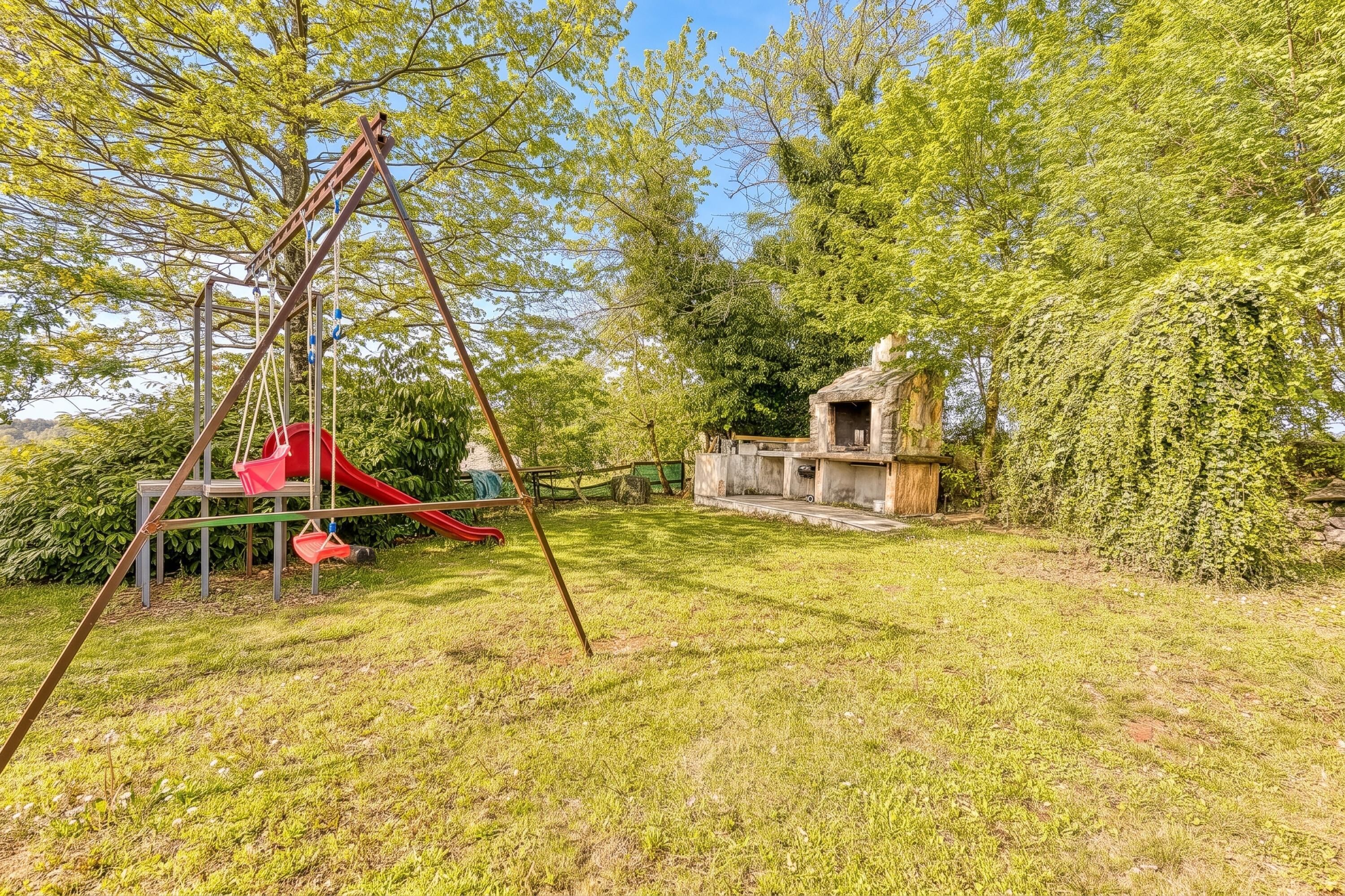 A playground with a swing set and slide, surrounded by trees and a small building.