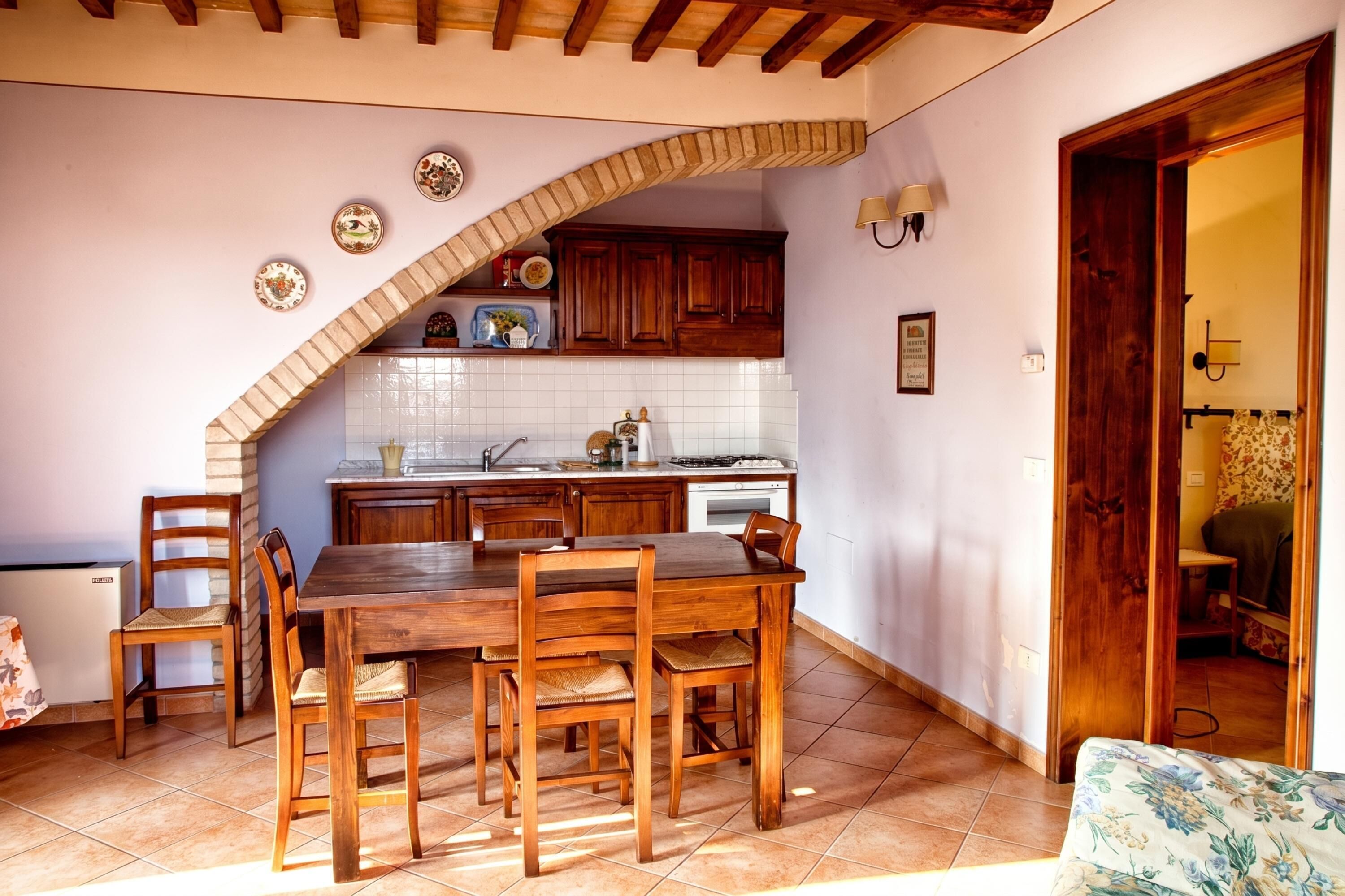 Una cocina con una mesa de comedor y sillas, armarios de madera, salpicadero de azulejos y techo de madera.