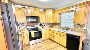 A kitchen with wooden cabinets, a stainless steel refrigerator, a black microwave, a stove, and a dishwasher. - Vette City retreat convenient to Mammoth Caves, Beech Bend, NCM, WKU. (Bowling Green)