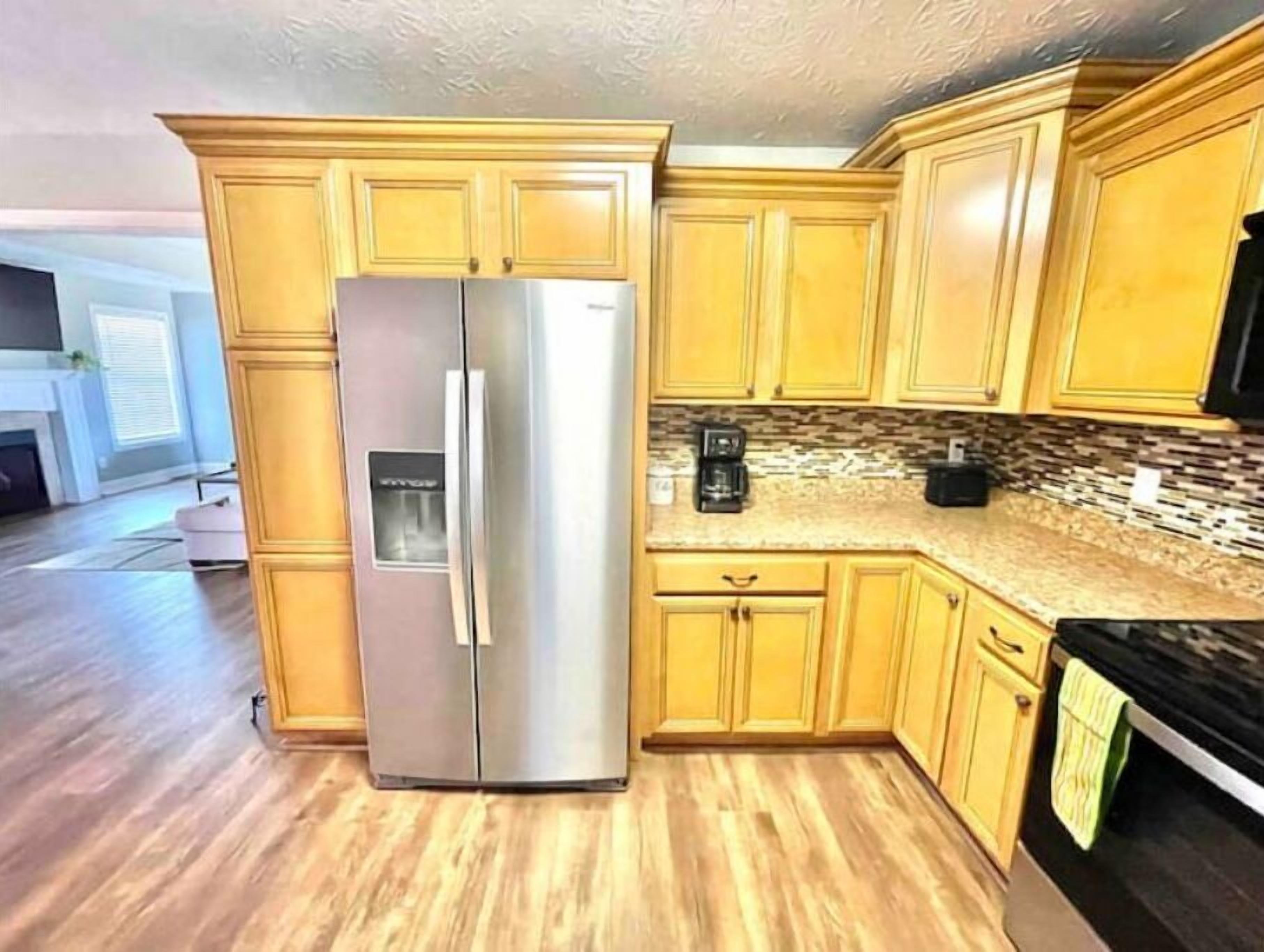 A kitchen with wooden cabinets, a stainless steel refrigerator, and a granite countertop.