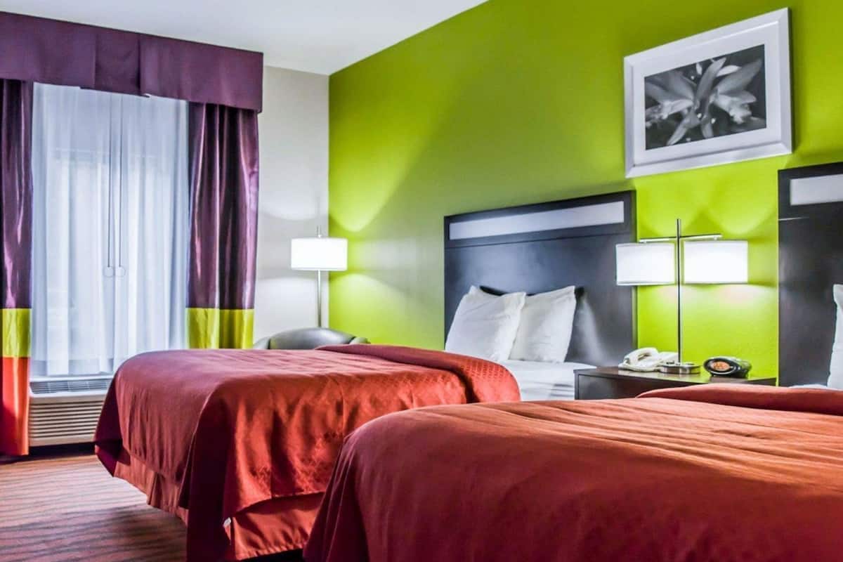 Ein Hotelzimmer mit zwei Betten, einem großen Fenster mit Vorhängen, einer grünen Akzentwand und einem gerahmten Bild an der Wand.