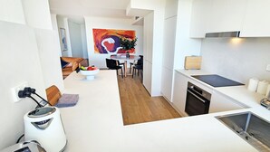 Una cucina moderna con mobili bianchi, un piano di lavoro nero e un lavello in acciaio inossidabile. C'è un'area pranzo con un tavolo rotondo e sedie, e un quadro astratto colorato appeso al muro.