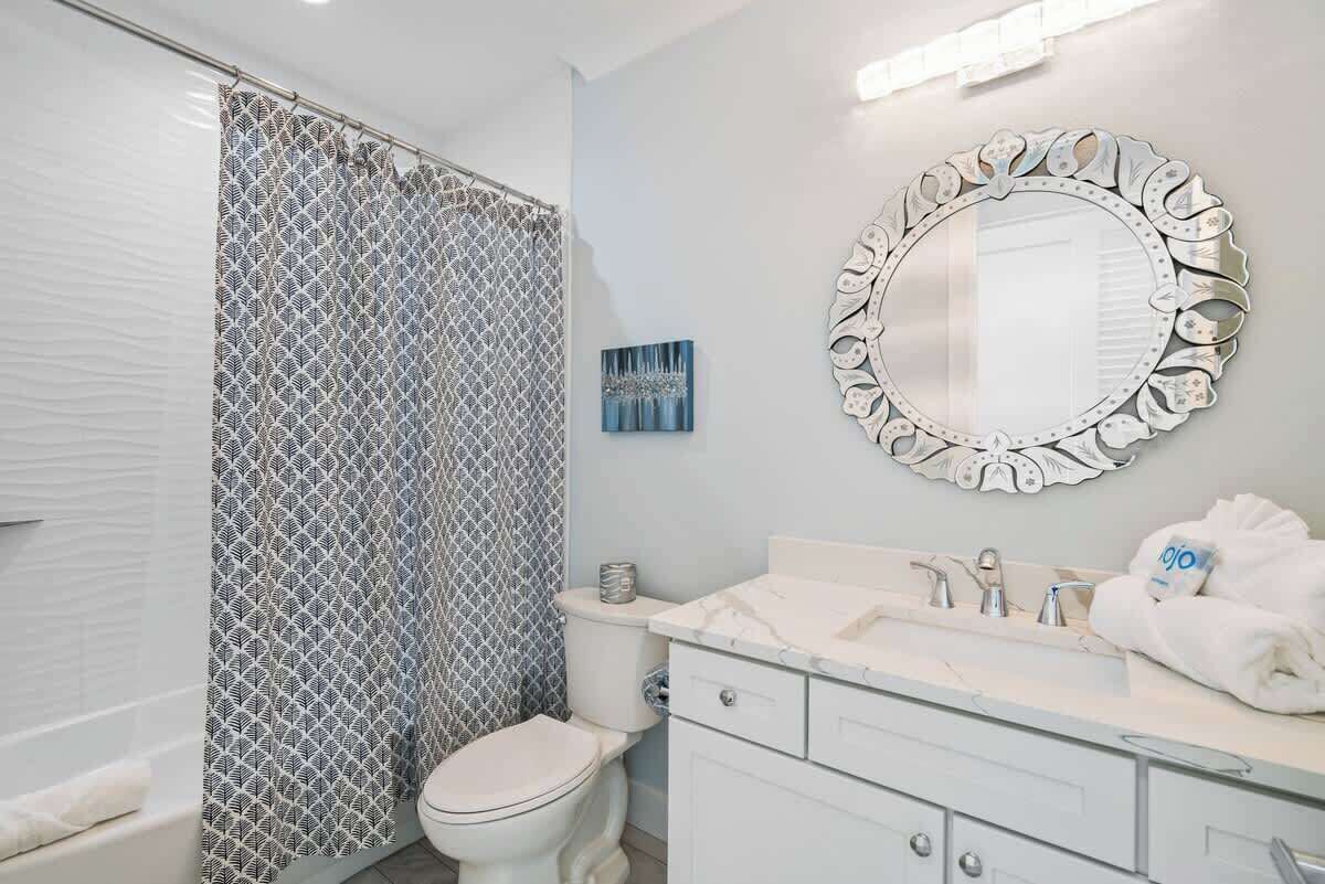 A bathroom with a shower curtain, toilet, sink, and a decorative mirror.