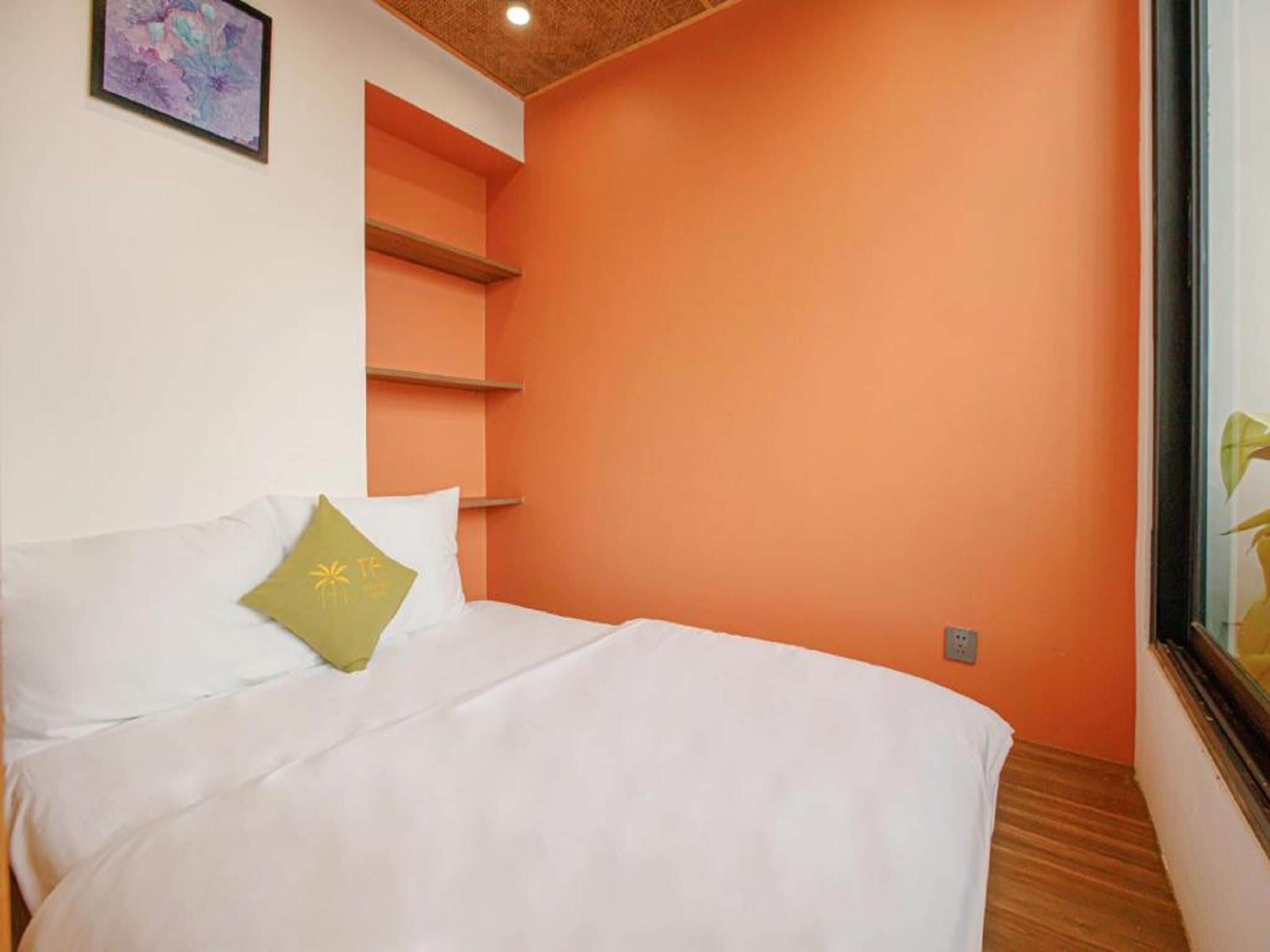 A bedroom with a bed, a green pillow, and orange walls.