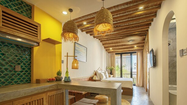 Een moderne keuken met een houten aanrecht, een zithoek met krukken, en een slaapkamer met een groot bed en uitzicht door een raam.