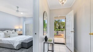 A bedroom with a bed, bedside table, and a view of the garden through an open door. - The OC Home: Centrally Located, Home Away Home (Coconut Grove)